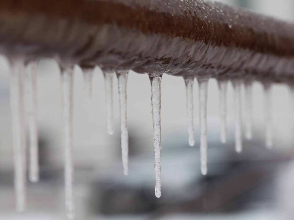 Icicles hanging from a brown pipe. Frozen water and metal surface, winter time concept. selective focus shallow depth of field